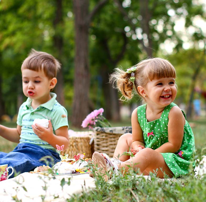 Caucasian little boy and girl eating sweets in the park