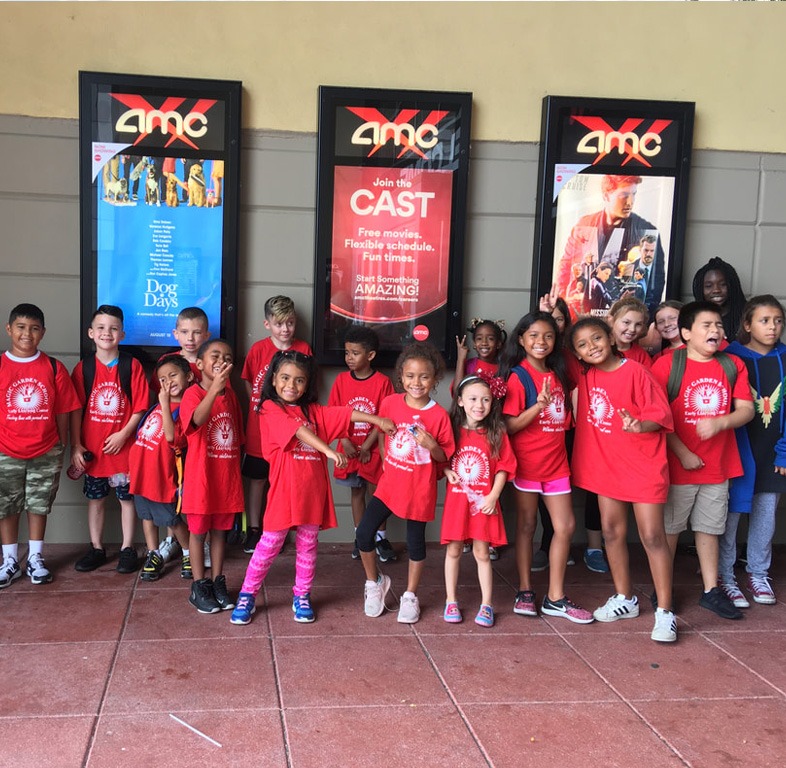 A diverse group of children wearing matching red t-shirts poses together outside an AMC movie theater