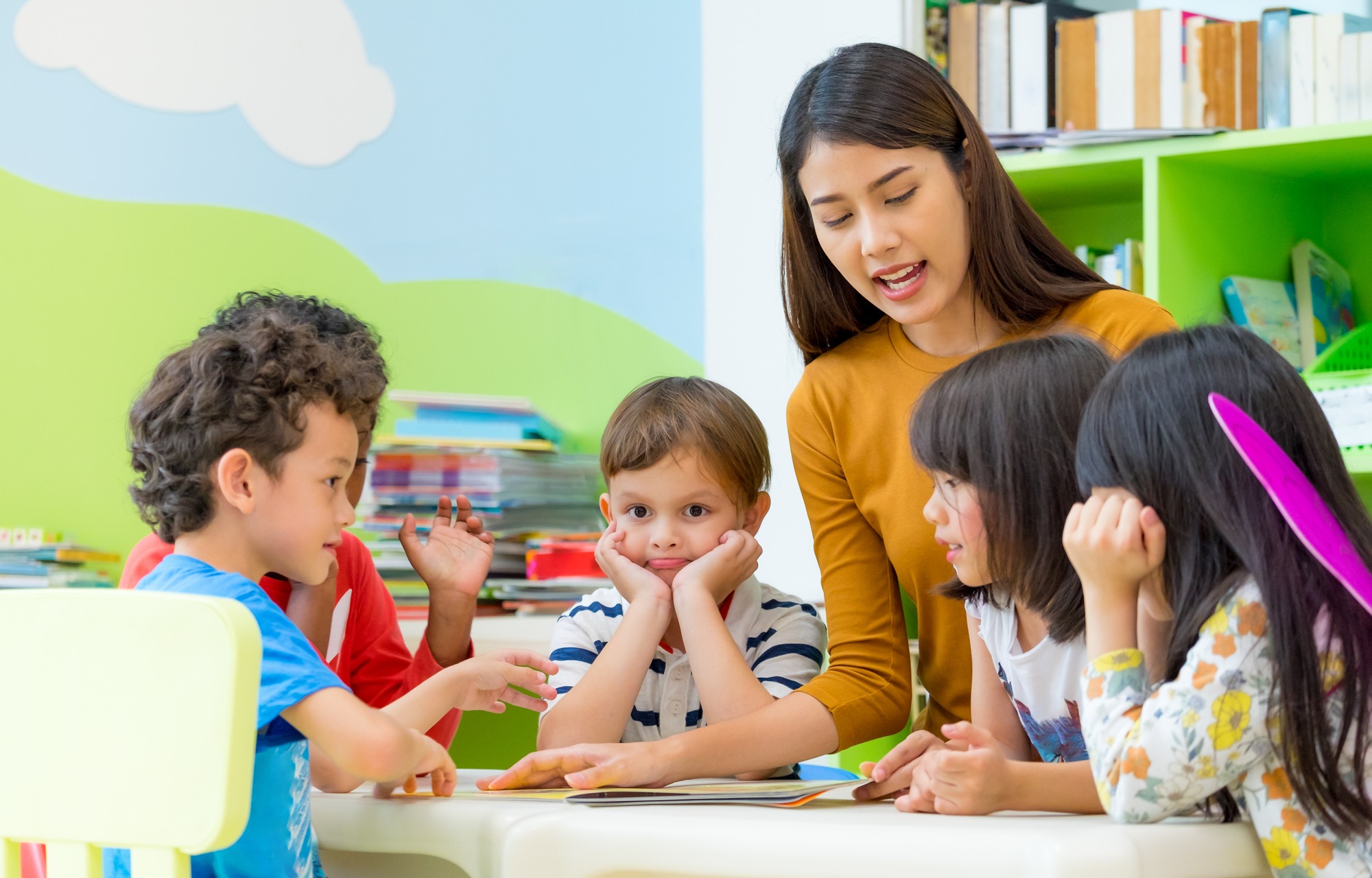 A teacher engages with four young children gathered around a table